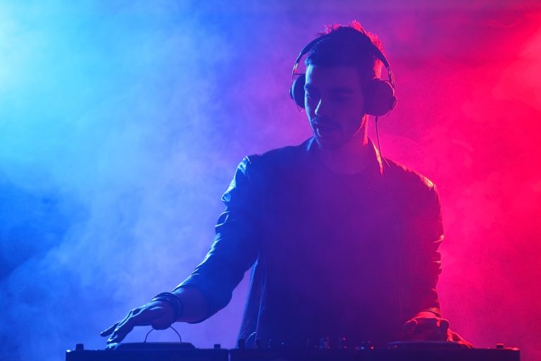 DJ playing music at mixer on colorful foggy background